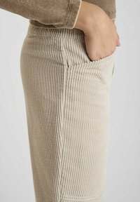 Beige corduroy broek met verticale ribbelstructuur, voorzien van een zijzak en een aansluitende pasvorm.