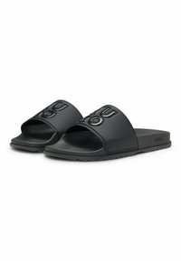 Black slide sandals made of rubber with a textured sole. Features a wide upper band with embossed "HUGO" logo. Flat design, open-toe style.