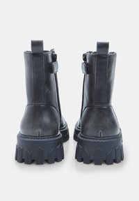 Botine negre din piele cu talpă groasă, fermoar lateral și detalii cu bucle. Materialul este neted cu un finisaj mat.