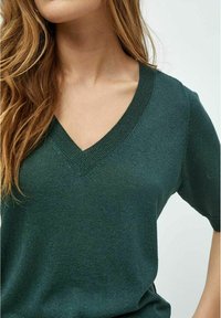 Suéter de pico verde oscuro hecho de un tejido de punto texturizado con mangas cortas y un cuello de canalé, que presenta un sutil brillo.