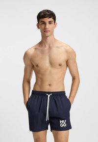 Marina shorts i marinblått med elastisk midja, vit dragsko och stor vit "HUGO" logotyp på vänster sida. Slätt, snabbtorkande tyg.