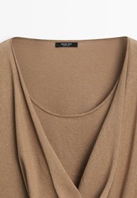 Beige stickad top med vid rund halsringning, draperad tygdetalj och en svart Massimo Dutti-etikett vid kragen.