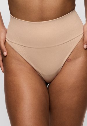 Beige naadloze ondergoed met hoge taille, gedragen op het middel en de bovenbenen van een persoon met een harttattoo op de rechterheup.