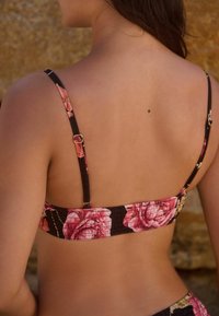 Kwiatowy top bikini na ciemnym tle, z regulowanymi ramiączkami i marszczeniami. Akcentowany różowymi różami i solidnymi akcesoriami.