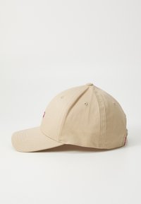 Beige pet gemaakt van katoen met een gebogen klep. Heeft een zes-panelenconstructie en een klein geborduurd logo aan de voorkant.