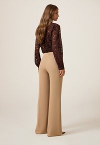 Bruine kanten lange mouwen top met bloempatronen, gecombineerd met hoge beige wijde broek, getoond vanuit een zij- en achteraanzicht.