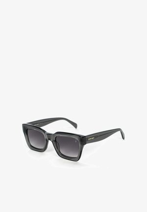 Zwarte rechthoekige zonnebril met een gradiënt van donkere lenzen, glanzende kunststof monturen en zijdetails in goud met het merk "SURI FREY."