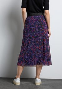 Midiklänning i genomskinligt tyg med intrikata lila och röda abstrakta mönster. Har ett svart elastiskt midjeband med präglad text.