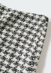 Gros plan d’un tissu tweed pied-de-poule noir et blanc avec un motif tissé texturé sur un fond clair.