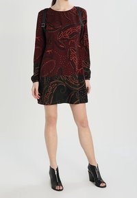 Abito a maniche lunghe in tessuto bordeaux con motivo paisley; orlo nero. Abbinato a stivaletti neri alla caviglia con cerniere. Dettaglio di design testurizzato.
