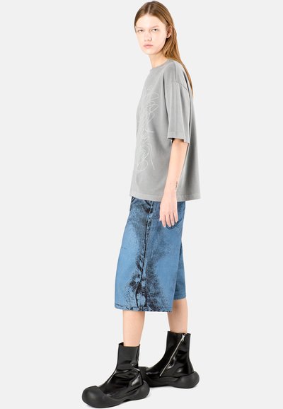 Gray oversized t-shirt with abstract white line design, paired with knee-length denim shorts featuring a textured blue pattern and black zip boots.