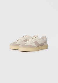 Beige suede sneakers with a cream textured overlay, round toe, and flat lace-up design. Thick rubber soles provide cushioning and support.