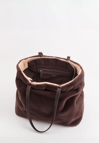 Sac cabas en peluche marron avec doublure intérieure douce, deux anses d'épaule et une poche zippée à l'intérieur. Forme arrondie avec un haut froncé.