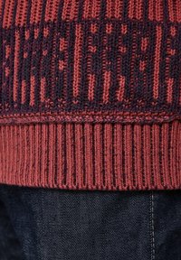 Gestrickter roter und dunkelblauer Pulloverboden mit geripptem Muster. Deutliche horizontale Streifen bilden ein Muster. Weicher, strukturierter Stoff sichtbar.