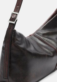 Borsa a spalla in pelle nera con un design morbido, caratterizzata da un accento bordeaux e una fibbia in metallo argento sul manico.