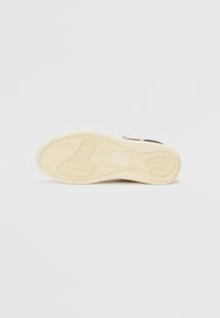 Semelle d'une basket décontractée beige avec des motifs d'adhérence texturés et un design en zigzag sur un fond clair uni.