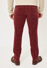 Braune Cordhosen mit strukturierter Oberfläche. Verfügen über zwei Gesäßtaschen mit Ziernähten. Kombiniert mit braunen Schuhen und einem beigen Oberteil.