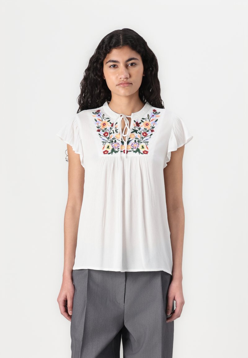 Blouse blanche avec broderie florale multicolore, encolure ronde avec détail de lien, manches courtes à volants et texture plissée.