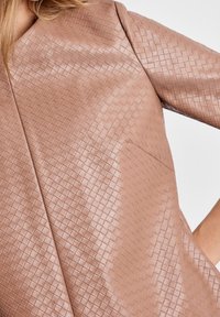 Prenda de cuero rosa texturizado que presenta un patrón tejido y un corte holgado. El escote en V y las mangas amplias realzan su diseño distintivo.
