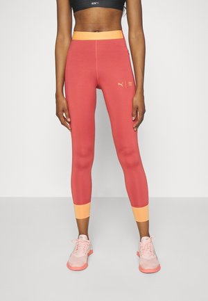 Leggings de sport PUMA en corail, avec une ceinture orange portant du texte. Longueur sous le genou avec un accent orange au niveau des poignets.