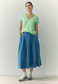 Roheline V-kaelusega T-särk lühikeste varrukatega, sobitatud teksase maksiseelikuga. Komplekti kuuluvad hallid tossud ja valged pahkluu sokid.