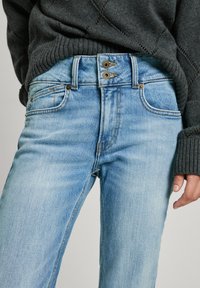 Ljust blåkorniga jeans med en klassisk femfickdesign, tvåknappslås och subtila urtvättningar, tillsammans med en mörk, texturerad tröja.