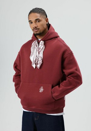 Bordeauxrode hoodie met een voorzak, geribbelde boorden en zoom. Heeft een witte sjaal met patroon, vastgeknoopt aan de hals, en een logo op de zak.