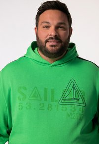 Sudadera con capucha verde con un gráfico de un velero y texto. Cuenta con un capuchón con cordones, textura suave y acentos negros en los lados.