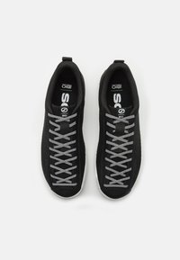 Svarte strikkede joggesko med grå snørebånd, hvite såler og logo på tungen. Lett vekt, pustende stoff med en teksturert overflate.