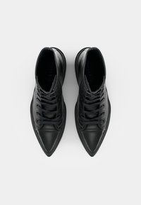 Zwarte enkelboots met een puntige neus, vervaardigd uit leer, en met een platte rubberen zool. Voorzien van oogjes en veters.