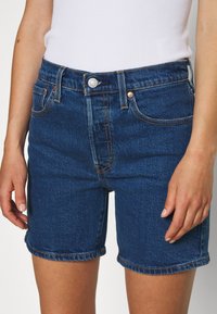 Denim shorts in dark blue, featuring a classic cut, five pockets, and contrast stitching. The fabric is smooth with an even texture.
