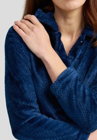 Sudadera de felpa azul marino con patrones texturizados, cuello con cremallera y un acabado de tela suave. Las mangas son ligeramente holgadas.