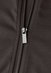 Tela gris oscuro con textura lisa, con una cremallera metálica en el centro, lengüeta de extracción plateada y costuras en zigzag prominentes en los bordes.