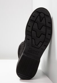 Černá gumová podrážka tenisky s texturovanými gripovými vzory. Obsahuje branding "TOMMY JEANS" a velikost 42. Úhlový, plochý design vhodný pro volnočasové nošení.