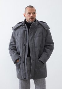 Abrigo gris acolchado con capucha, con cierres de botones, bolsillos frontales y un diseño acolchado, complementado con un cuello alto.