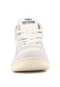 Vue de face d'une sneaker Palladium beige et blanche avec lacets et étiquette de marque sur une arrière-plan blanc.
