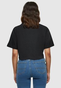 Tricou negru scurt cu mâneci scurte, asociat cu blugi din denim albastru, ajustați, cu buzunare la spate și cusături subtile.