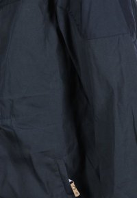 Giacca blu scuro realizzata in tessuto leggero. Caratterizzata da una tasca con zip, una trama fine e un piccolo dettaglio in pelle con bottone.