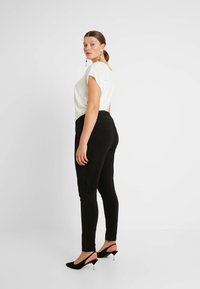 Biała bluzka z krótkim rękawem w połączeniu z czarnymi, dopasowanymi spodniami. Stylistykę uzupełniają czarne czółenka na obcasie w formie slingback z wąskim obcasem.