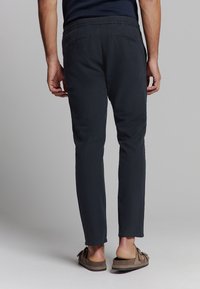 Marineblauwe broek met een slim fit, met een elastische tailleband en achterzakken, gemaakt van zachte stof, gecombineerd met bruine instappers.