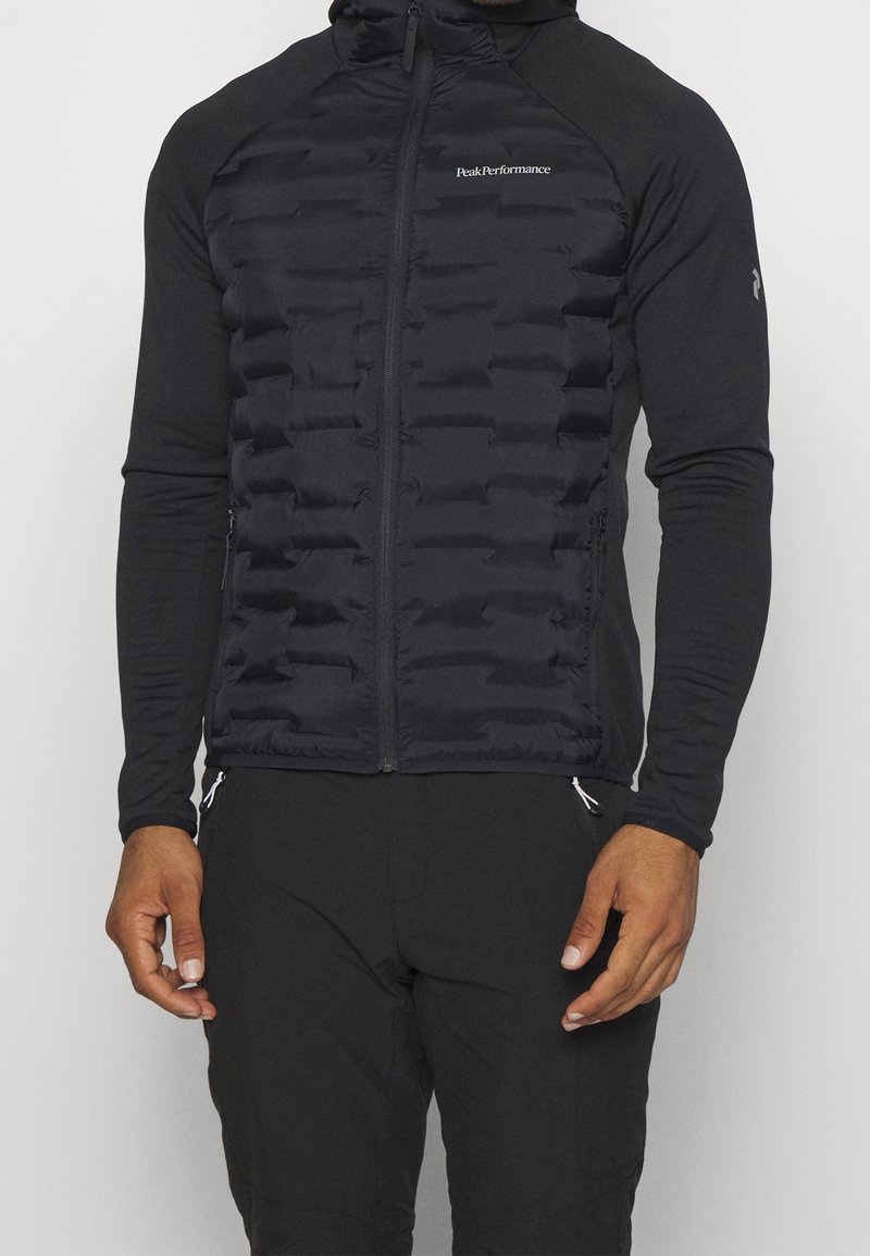 Veste noire rembourrée avec un col montant et une fermeture éclair, associée à de longues manches noires. Texture lisse avec un design élégant et ajusté.