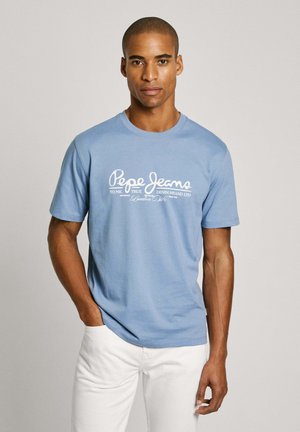 Lichtblauw katoen T-shirt met korte mouwen en een ronde hals, met in het midden een witte tekstlogo. Ggedragen met witte broek.