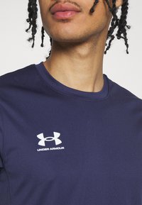 Námornícky modré športové tričko vyrobené z hladkej látky, s okrúhlym výstrihom a bielym logom Under Armour na hrudi.