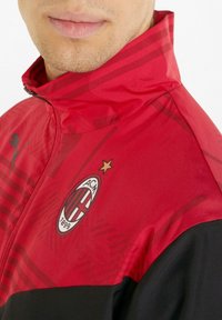 Rot und schwarze Sportjacke mit hohem Kragen, versehen mit einem Logo, Stern und einem dezenten Streifenmuster auf dem Stoff.