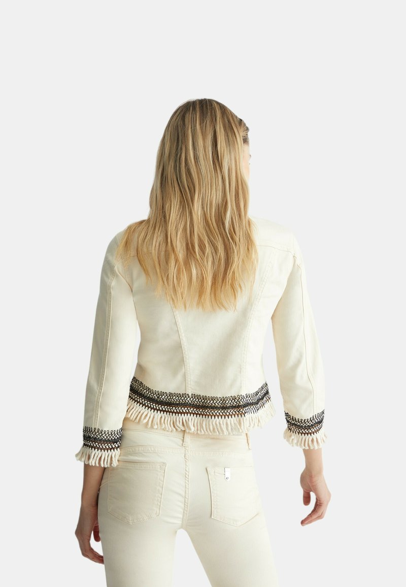 Veste en denim crème au design ajusté, avec des bordures brodées noires et des accents frangés au niveau de l'ourlet et des manches. Vue arrière présentée.
