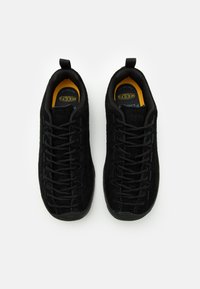 Czarne zamszowe sneakersy o streamlined designie, z okrągłym noskiem, grubymi czarnymi sznurówkami i teksturowaną gumową podeszwą. Akcent w postaci żółtej wkładki.