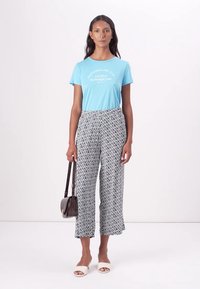 T-shirt blu a maniche corte con testo bianco, abbinato a culotte a fantasia bianco e nero. La modella porta una borsa a tracolla e indossa sandali bianchi.