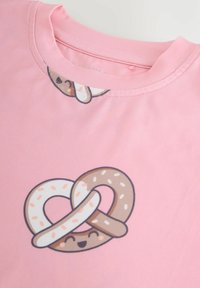 Maglietta rosa con una grafica di un pretzel allegro nei colori marrone e bianco, su un tessuto morbido.