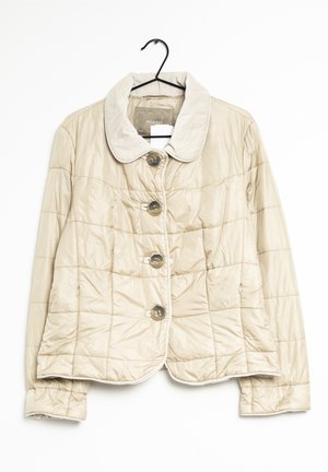 Beige quiltet jakke med store knapper, rund krave og lange ærmer, der hænger på en sort bøjle.