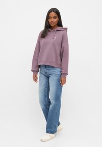 Lichtpaarse cropped hoodie met een trekkoord, gecombineerd met lichtblauwe wijde jeans en crèmekleurige sneakers. Eenvoudig en casual ontwerp.